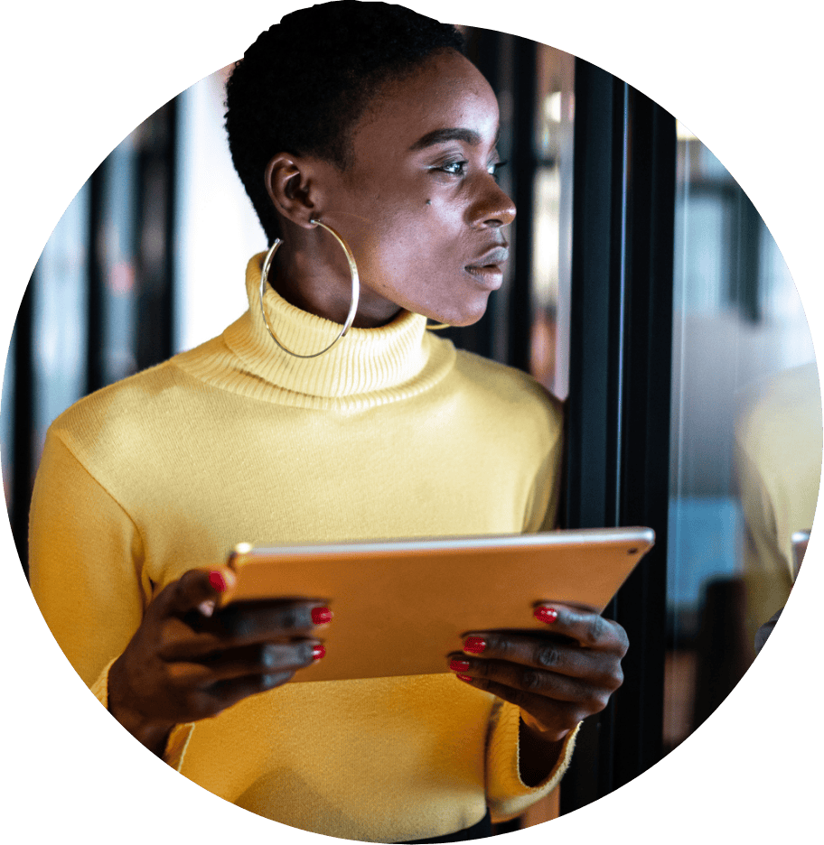 Woman holding tablet looks out of a window.