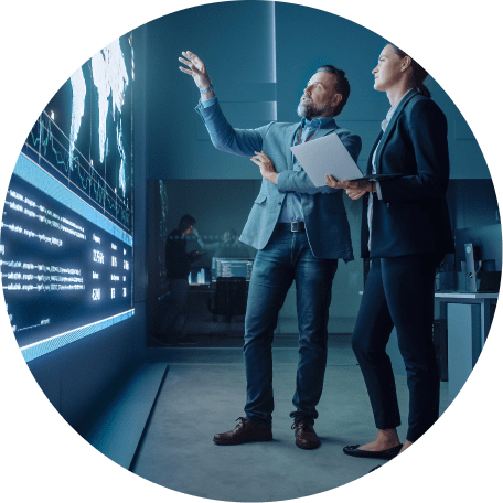 Man and woman have a discussion while looking at a large electronic display wall.