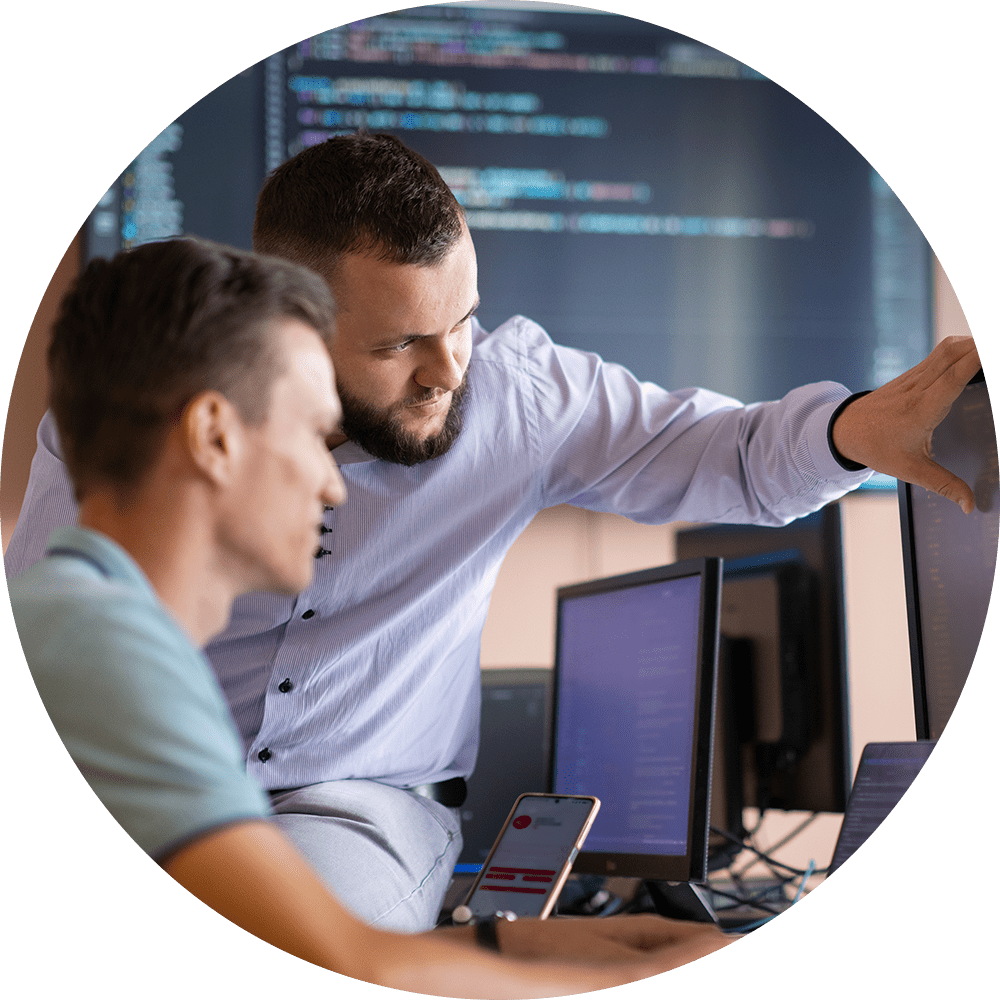 Co-workers review code on a large desktop computer screen.